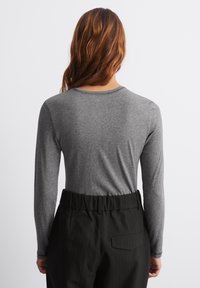 Bluză cu mâneci lungi, de culoare gri, cu decolteu rotund, textură netedă și croială lejeră, asociată cu pantaloni negri cu dungi verticale și talie înaltă.