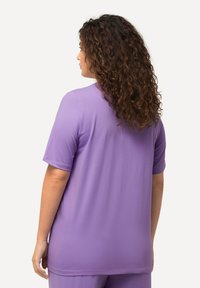 Camicetta viola a maniche corte realizzata in tessuto morbido con vestibilità rilassata. Presenta un collo rotondo e una consistenza morbida.