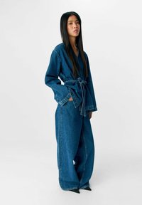 Denim jumpsuit met wijde broeken, lange mouwen en een ceintuur in de taille. Beschikt over een zachte textuur en een diepe blauwe kleur.