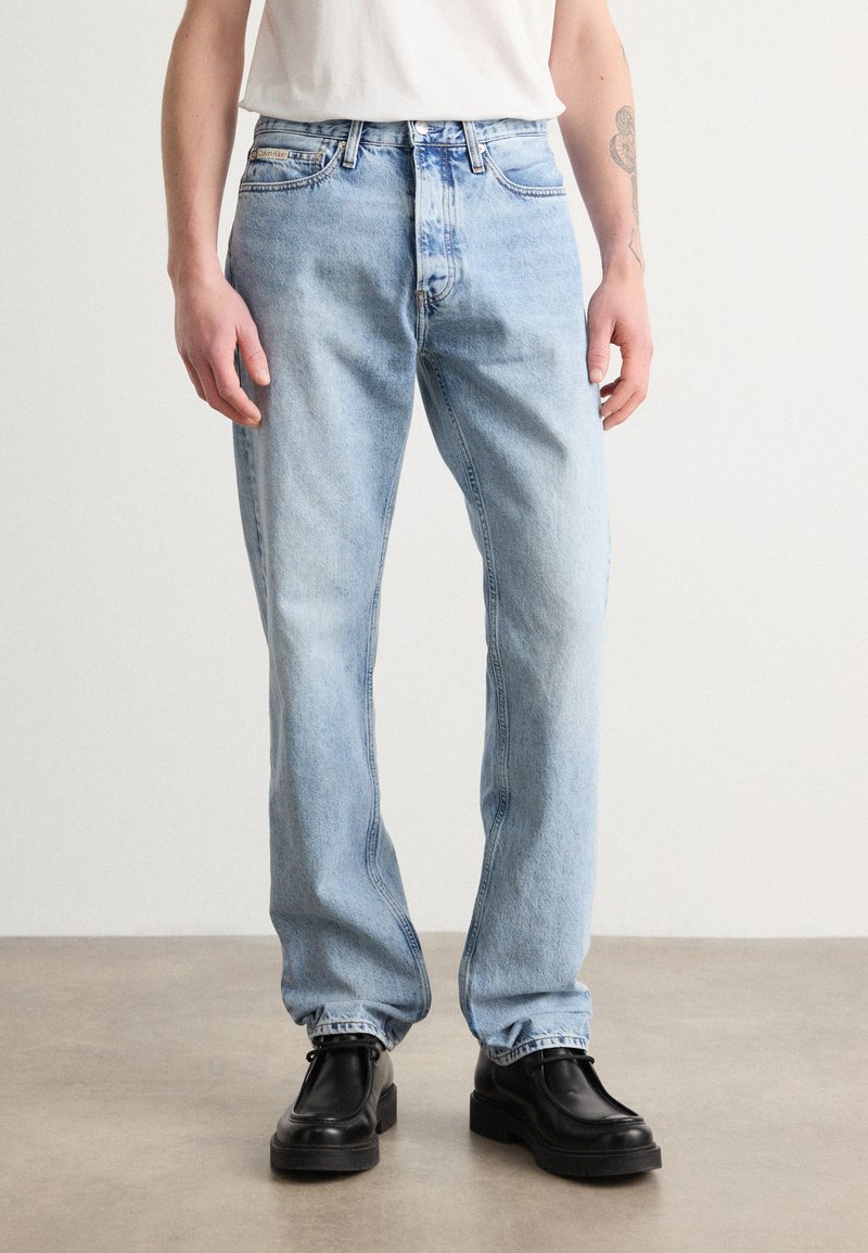 Vaqueros de mezclilla de color azul claro con un ajuste holgado y pierna recta. Presenta un diseño estándar de cinco bolsillos y costuras en contraste. Llevados con zapatos negros.