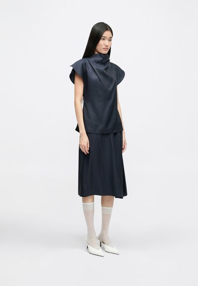 Navy top with a cowl neckline and short, structured sleeves, paired with a matching full skirt. White heeled mules and sheer socks complete the look.