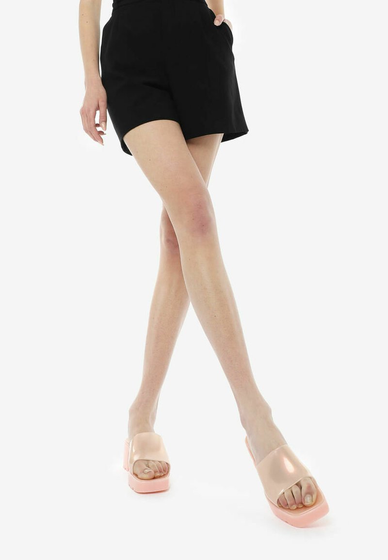 Duidelijke roze platform sandalen met een glanzende afwerking, met een open teen en een breed bandontwerp, gecombineerd met zwarte shorts.