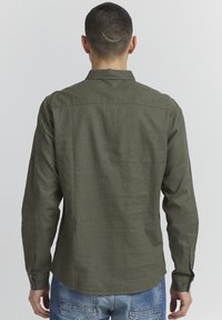 Olive green long-sleeve shirt made of lightweight fabric. Features a straight hem, buttoned cuffs, and a plain back design.