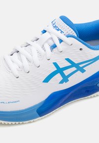 Sapatilha atlética branca com detalhes azuis, apresentando um upper texturizado, um logótipo azul proeminente e uma sola azul. Os atacadores e o colar acolchoado são brancos.