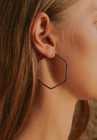 Schwarze Metall-Hexa-Ohrringe mit dünnem, minimalistischem Design. Zarte Glanzoberfläche, leicht und hängen an einem kleinen goldfarbenen Stecker.
