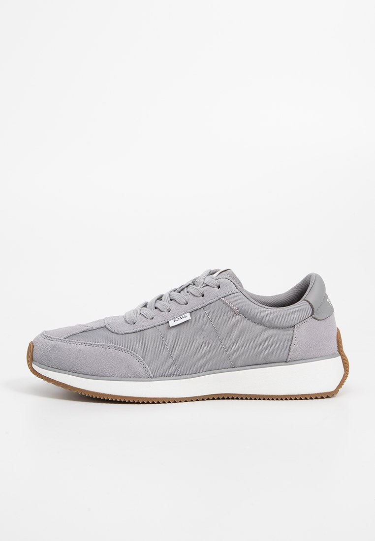 Baskets grises avec un dessus en tissu et en daim, conçues avec un bout arrondi, une semelle intermédiaire blanche et une semelle extérieure en caoutchouc marron. Comprend un système de laçage.