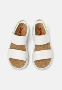 Vita sandaler med två breda remmar och korkinsoles. Har en rund tå och texturerad yta, med ett varumärke i röd färg på insolen.