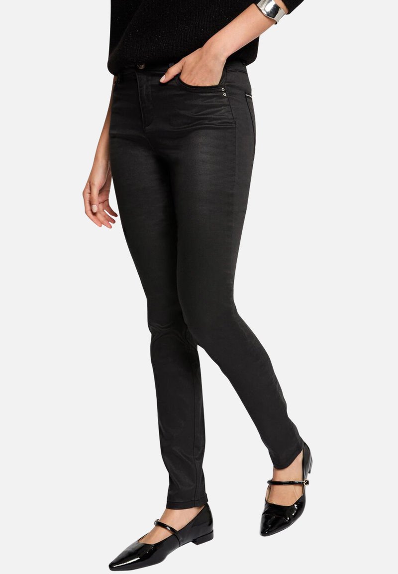 Jeans elásticos negros con corte ajustado, que cuentan con bolsillos frontales y una textura suave. Combinados con zapatos planos negros para un look elegante.