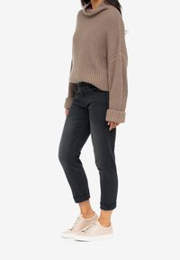 Beige stickad tröja med krage, i kombination med mörka uppvikta jeans och ljusbeige sneakers med snörning och vit sula.