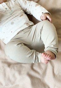 Leggings pour bébé de couleur beige clair en tissu doux, dotés d'un design ajusté avec des motifs texturés, associés à un haut à manches longues imprimé.