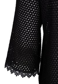 Tissu en crochet noir avec un bord en dentelle festonné formant une manche, présentant un motif de petits trous ouverts sur toute la surface.