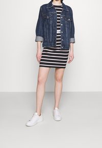 Jeansowa kurtka z podwiniętymi rękawami na czarno-białą w paski sukienkę. Białe sneakersy dopełniają stylizację. Gładkie tekstury i casualowy fason.