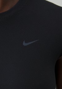 Svart ribbat träningslinne med rund halsringning och korta ärmar, med en liten grå Nike-logotyp fram.