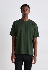 T-shirt en coton à manches courtes, de couleur vert foncé, avec un col ras du cou et un logo "BOSS" brodé subtilement à l'avant. Coupe décontractée et texture douce.