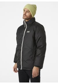 Chaqueta de plumas negra con aislamiento, cuello alto, cremallera blanca y puños elásticos. Combinada con un gorro de punto verde claro.