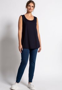 Námornícky bezrukávový top s okrúhlym výstrihom, skombinovaný s tmavomodrými slim-fit džínsami a bielymi teniskami. Hladká tkanina, voľný strih.