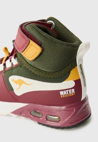 Sneaker wysoki z bordowym wykończeniem, zieloną tkaniną, żółtymi akcentami i etykietą "ODPORNY NA WODĘ" z boku. Widoczne szczegóły tekstury.