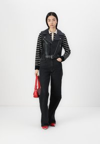 Black leather vest over a striped long-sleeve shirt, paired with high-waisted black jeans. Red handbag and red-accented shoes complete the look.