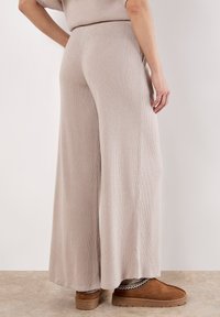 Lichtbeige ribbelige wijde broek gemaakt van zacht materiaal, met een hoge taille en subtiele textuur, gecombineerd met bruine instapschoenen.