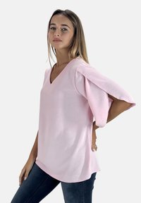 Roze V-hals top met pofmouwen, gemaakt van zachte stof. Kenmerken zijn een ontspannen pasvorm, een gebogen zoom en een gladde textuur. Gepaard met donkere jeans.