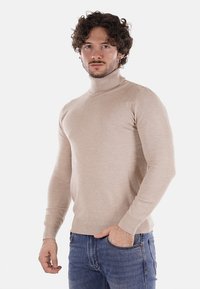 Maglione color beige a collo alto realizzato in morbido tessuto a maglia leggero. Design aderente con polsini e orlo a coste, abbinato a jeans di denim blu.