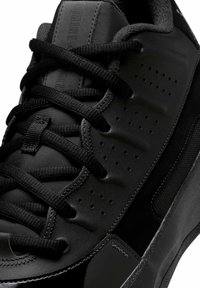 Scarpa sportiva nera con tomaia liscia, pannello testurizzato, perforazioni e lacci neri, con un accento lucido sulla punta.