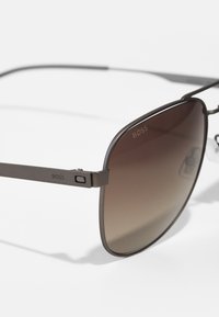 Occhiali da sole con lenti a gradiente scuro, montatura in metallo grigio e discreto marchio "BOSS" sulle aste. Design leggero e angolare.