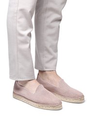 Voeten in lichtroze instap-espadrilles met geweven jutezolen, gecombineerd met lichtbeige cropped pants.