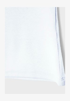 Zbliżenie na róg białej tkaniny z widocznym szwem i zagiętym brzegiem na jednolitym tle.