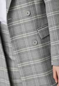 Blazer a quadri grigi con evidenti check bianchi e neri, dotato di due bottoni e una consistenza liscia e sartoriale con revers classico.