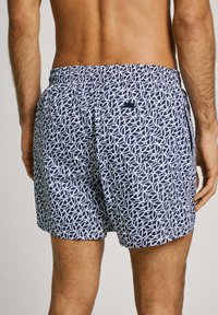 Pantaloni da bagno navy con un motivo geometrico bianco, cintura elastica e una tasca posteriore. Realizzati in un materiale leggero e a asciugatura rapida.