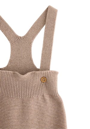 Strikket beige overall med brede stropper, ribbet tekstur ved taljen og en trækknapdetalje på siden.