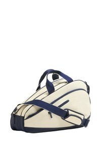 Kermanvärinen duffel-laukku, jossa tummansinisiä yksityiskohtia, kaksinkertaiset kahvat, irrotettava olkahihna ja vetoketjulliset osastot.