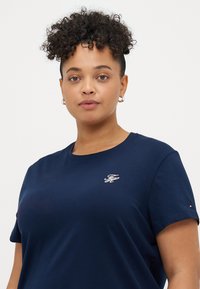 Navyblå bomulds T-shirt med korte ærmer, rund halsudskæring og hvid broderet logo på brystet. Diskret tekstur, afslappet pasform.