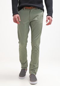 Gröna slim-fit chinos i lätt tyg, med en mjuk textur och framfickor, i kombination med grå slip-on skor.