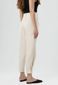 Hosen in Cremefarbe mit schmal zulaufender Form, Seitentaschen und einem umgeschlagenen Saum, kombiniert mit schwarzen Slip-On-Schuhen.