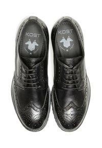 Chaussures en cuir noir avec une texture lisse, design à bouts ailés, détails perforés et lacets traditionnels. Présente le logo de la marque sur les semelles intérieures.