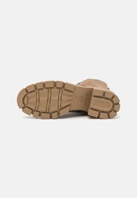 Suela de bota en color marrón claro con un patrón de tracción grueso y resistente. El material parece duradero, con estrías y una impresión de logo. Diseño de tacón plano.