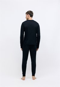 Top negro de manga larga y pantalones a juego, confeccionados en un tejido suave. El top tiene un corte recto; los pantalones presentan puños elásticos y un ajuste relajado.