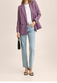 Blazer à carreaux violet porté sur un haut blanc, associé à un jean bleu clair à jambes droites et des sandales noires à lanières. Tenant un sac à main noir.