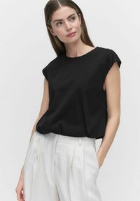 Czarny krótki top z luźnym krojem. Wykonany z miękkiego materiału, z okrągłym dekoltem i gładkim, minimalistycznym wzornictwem. Zestawiony z białymi spodniami.