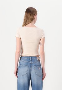 Maglietta aderente beige a maniche corte con scollatura rotonda, abbinata a jeans in denim blu chiaro a vita alta con una toppa e tasche posteriori ben definite.