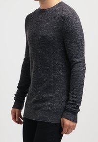 Pull en maille gris foncé avec manches longues, col rond, tissu texturé et poignets avec un design côtelé. Motif subtil à pois.