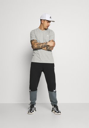 Camiseta gris con logo, pantalones jogger en negro y gris con detalles de acento, gorra blanca con logo y zapatillas deportivas negras.