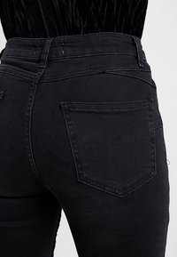 Svarta denimjeans med hög midja och figurnära passform. Har en bakficka och diskret sömnad. Slät textur.