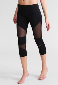 Leggings capri noirs avec panneaux en mesh sur les cuisses, une taille large et une coupe ajustée, présentant une texture de tissu lisse.