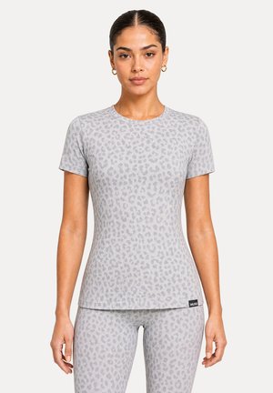 Femme portant un t-shirt manches courtes et des leggings assortis gris clair à imprimé léopard, debout face à l’avant avec une expression neutre.