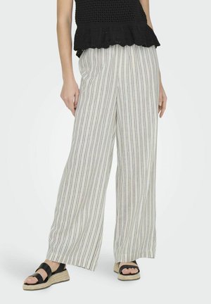 Pantalons légers à jambes larges avec un motif rayé, présentant une base crème avec des lignes bleues et rouges, associés à des sandales noires.