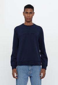 Sudadera azul marino de tejido suave, con cuello redondo, mangas largas y logotipo en relieve "MICHAEL KORS" en el frente.