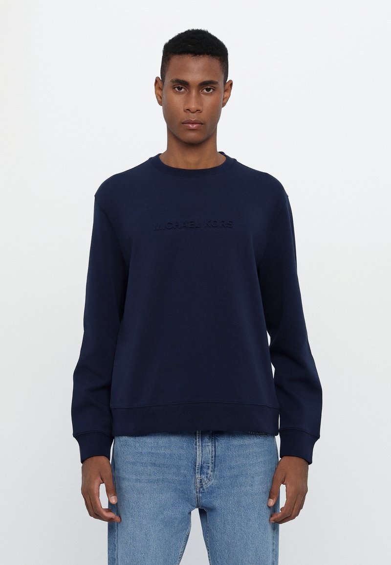Sudadera azul marino de tejido suave, con cuello redondo, mangas largas y logotipo en relieve "MICHAEL KORS" en el frente.